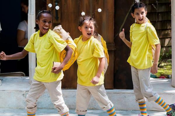 Three young actors in bee costumes, winking at the audience