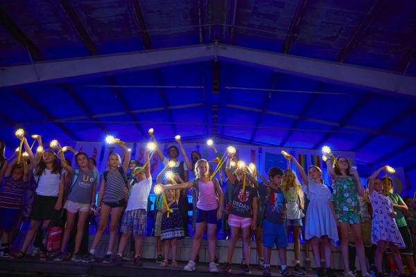 Children standing on stage holding lights and waving them in the air 