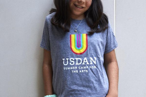 Young girl standing in Usdan t-shirt with rainbow U 