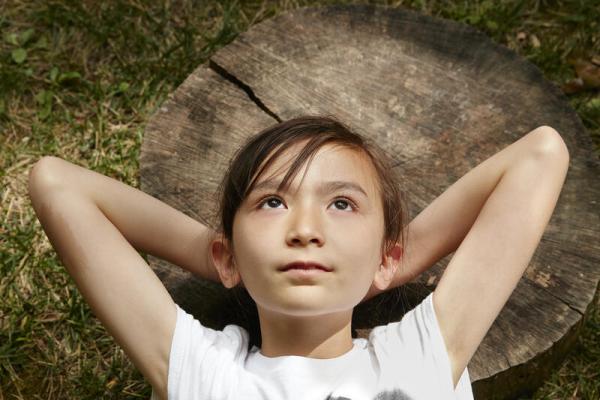 Young girl lying on a log with her hands behind her head
