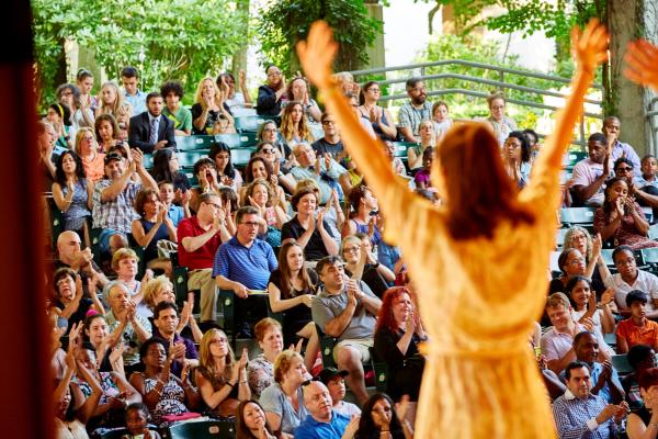 The back of a young performer on stage She is facing the audience with arms raised