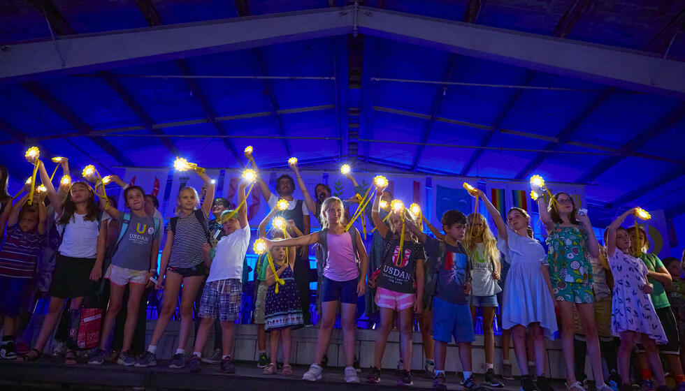 Children standing on stage holding lights and waving them in the air. 