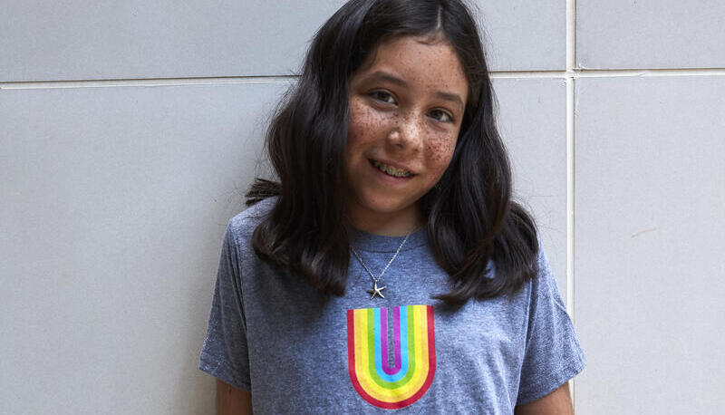 Young girl standing in Usdan t-shirt with rainbow U. 