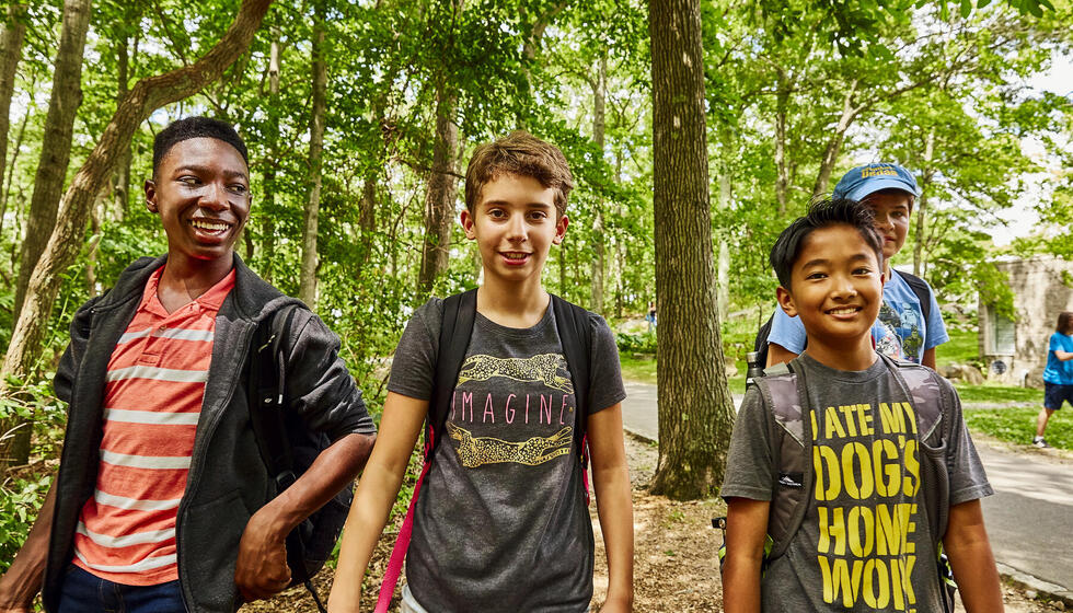 Three kids standing in the woods, smiling.