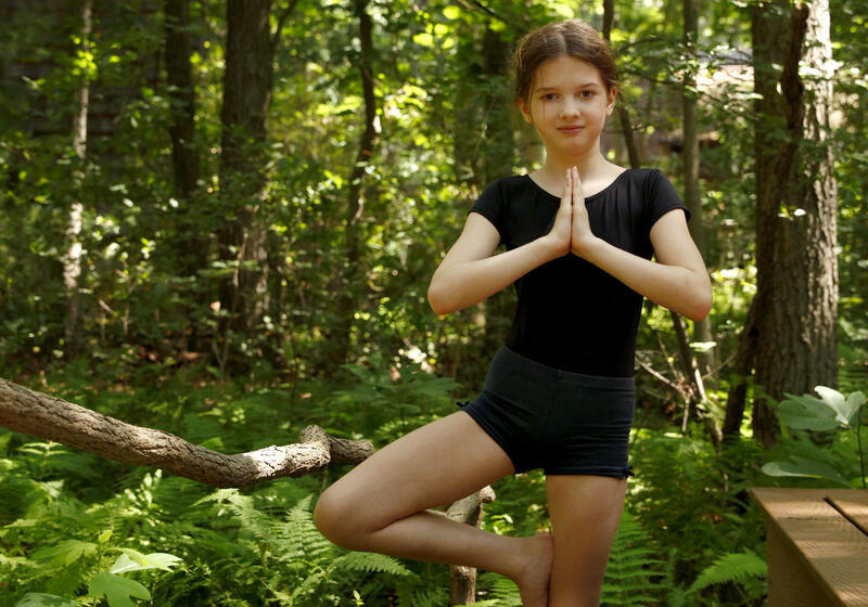 Young girl striking the Yoga Tree pose in the woods.