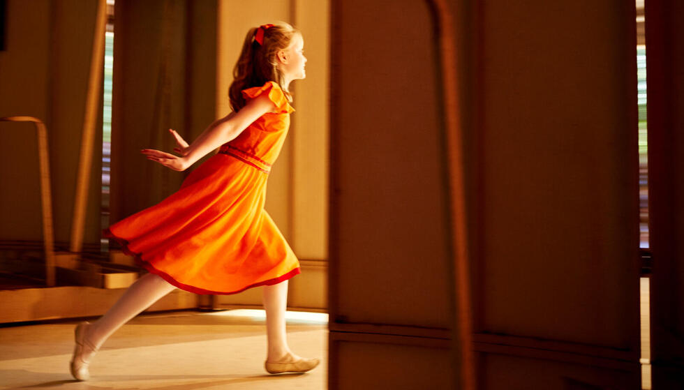 A young dancer in an orange dress running onto the Amphitheater stage.