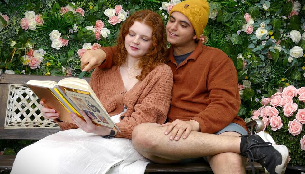 A couple sitting on a bench reading a book.