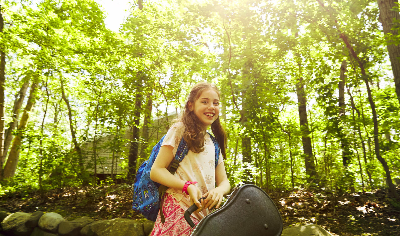 Student carrying a violin in the woods and smiling