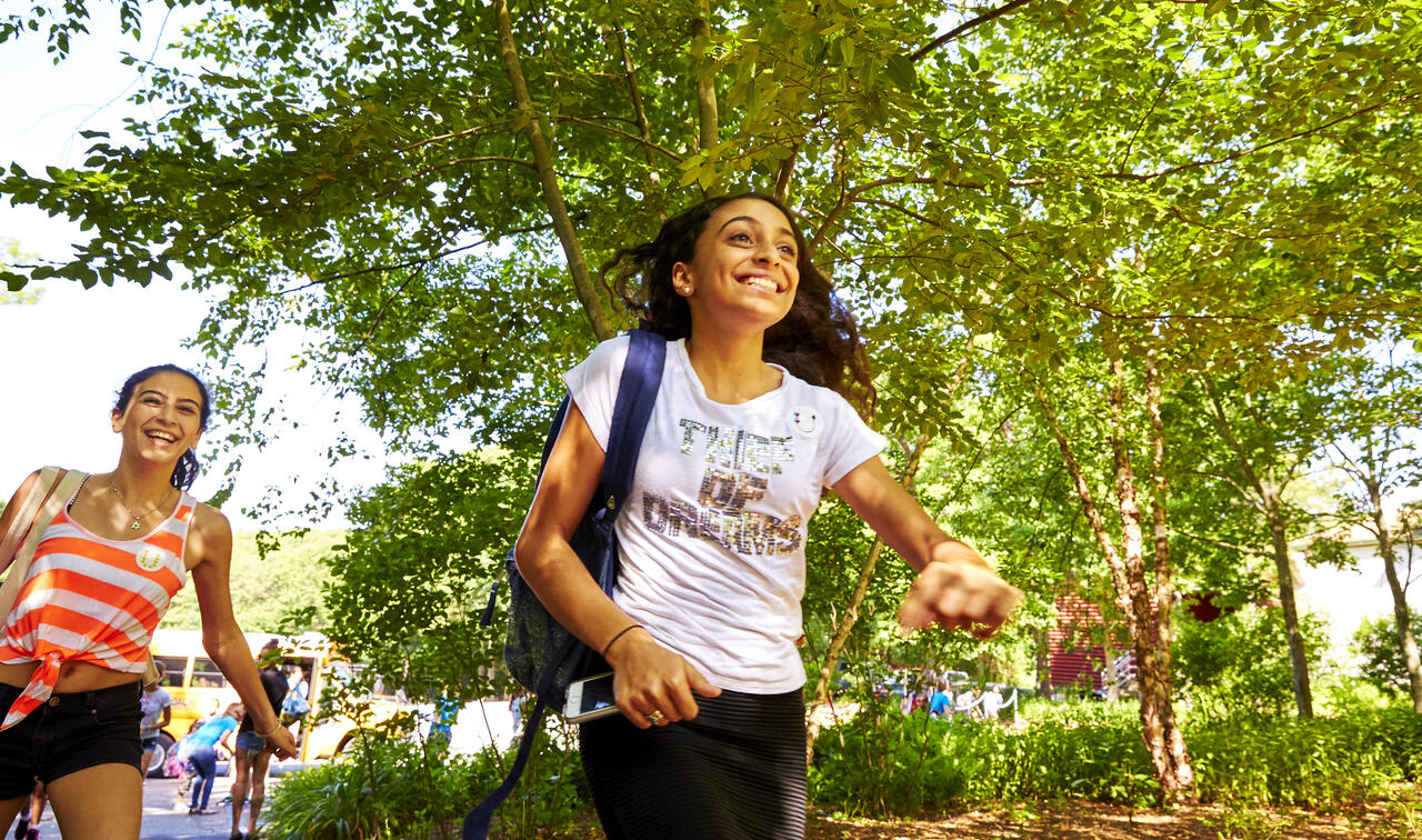 Girl running onto Usdan's campus smiling. 