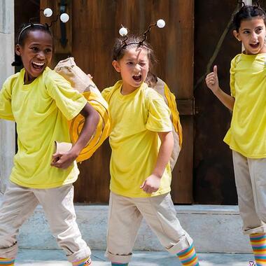 Three young actors in bee costumes, winking at the audience.