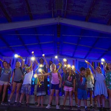 Children standing on stage holding lights and waving them in the air. Children standing on stage holding lights and waving them in the air.
