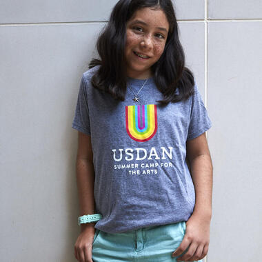 Young girl standing in Usdan t-shirt with rainbow U. Young girl standing in Usdan t-shirt with rainbow U.