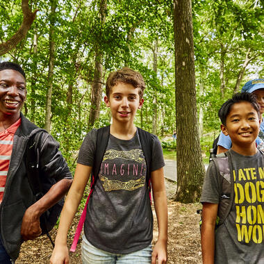 Three kids standing in the woods, smiling.
