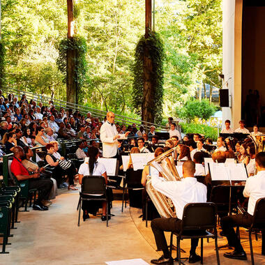 Music arts camp on Long Island. Conductor in front of band in Amphitheater surrounded by green nature.