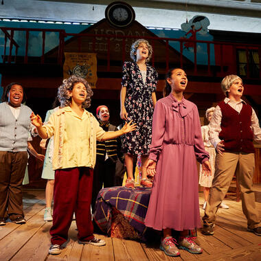 five students performing in costume on stage