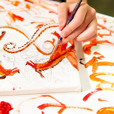 Closeup of child's hand painting an orange dragon on canvas. Closeup of child's hand painting an orange dragon on canvas.