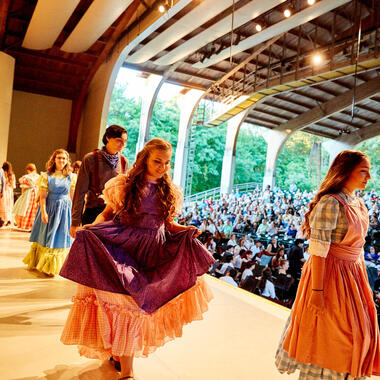 Group of students in costume proudly walking off the Amphitheater stage.