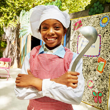 Young smiling girl dressed in a chef's costume and holding a ladle