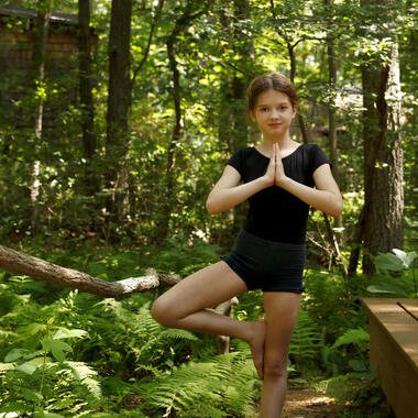Young girl striking the Yoga Tree pose in the woods.