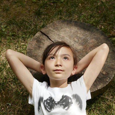 Young girl lying on a log with her hands behind her head.