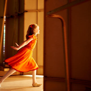 A young dancer in an orange dress running onto the Amphitheater stage. A young dancer in an orange dress running onto the Amphitheater stage.