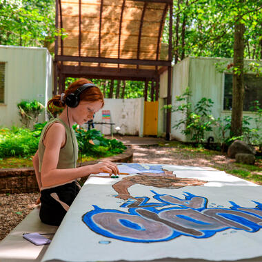 Student sitting in the woods painting and listening to music. Student sitting in the woods painting and listening to music.